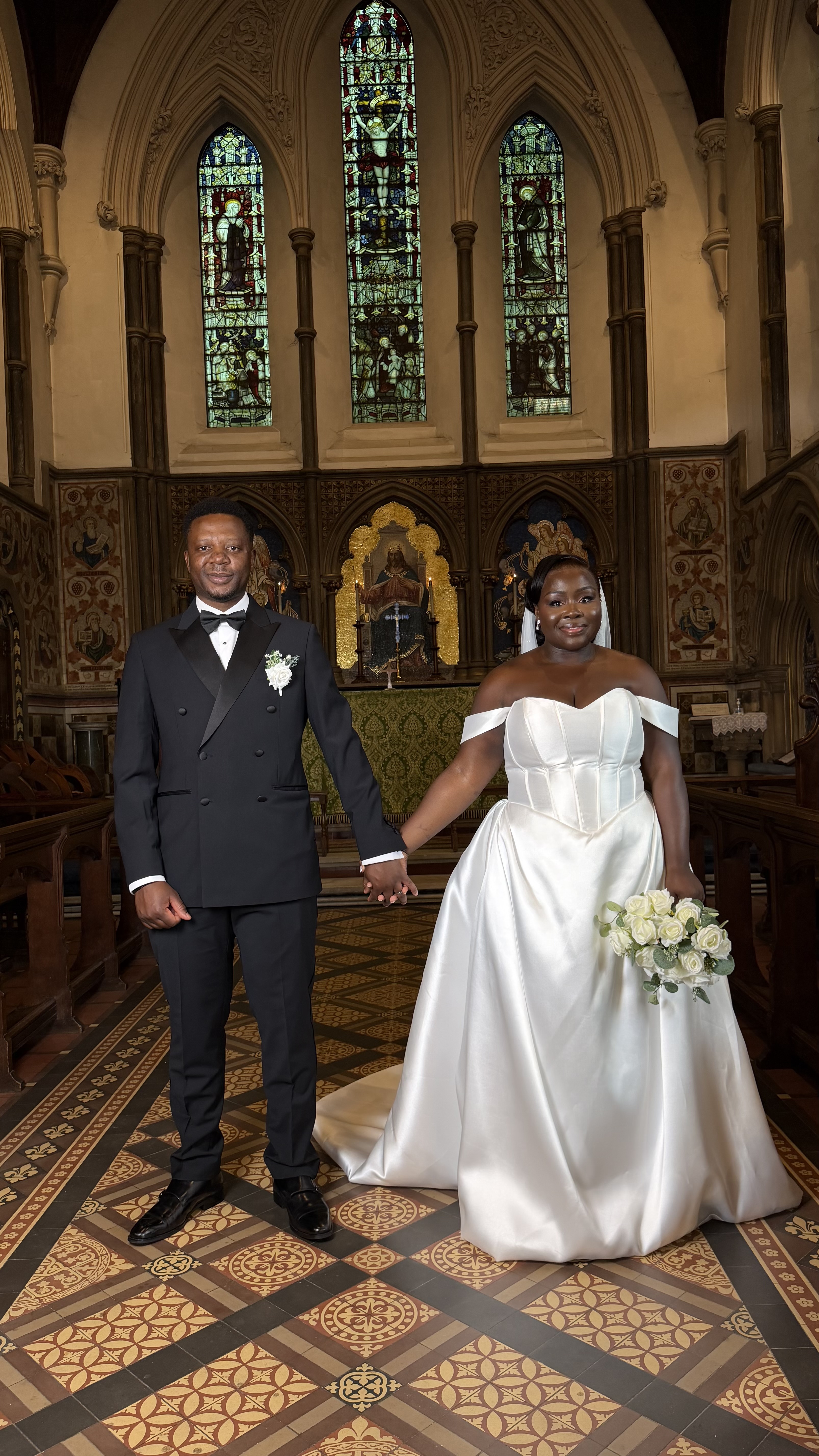 A bride and groom holding hands beneath stained-glass windows in a church