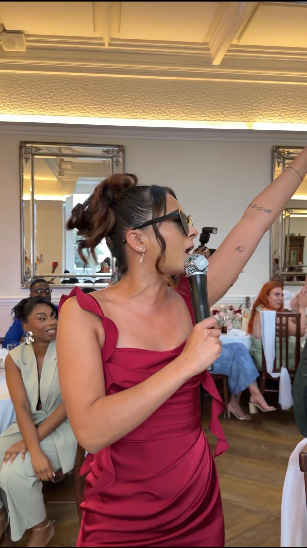 A wedding guest in a red dress singing into a microphone at the reception