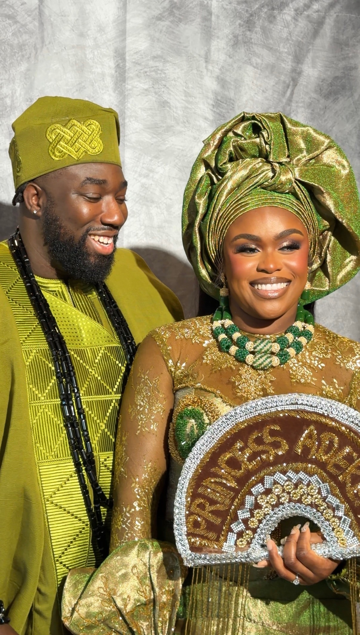 A bride and groom smiling in green and gold traditional wedding outfits