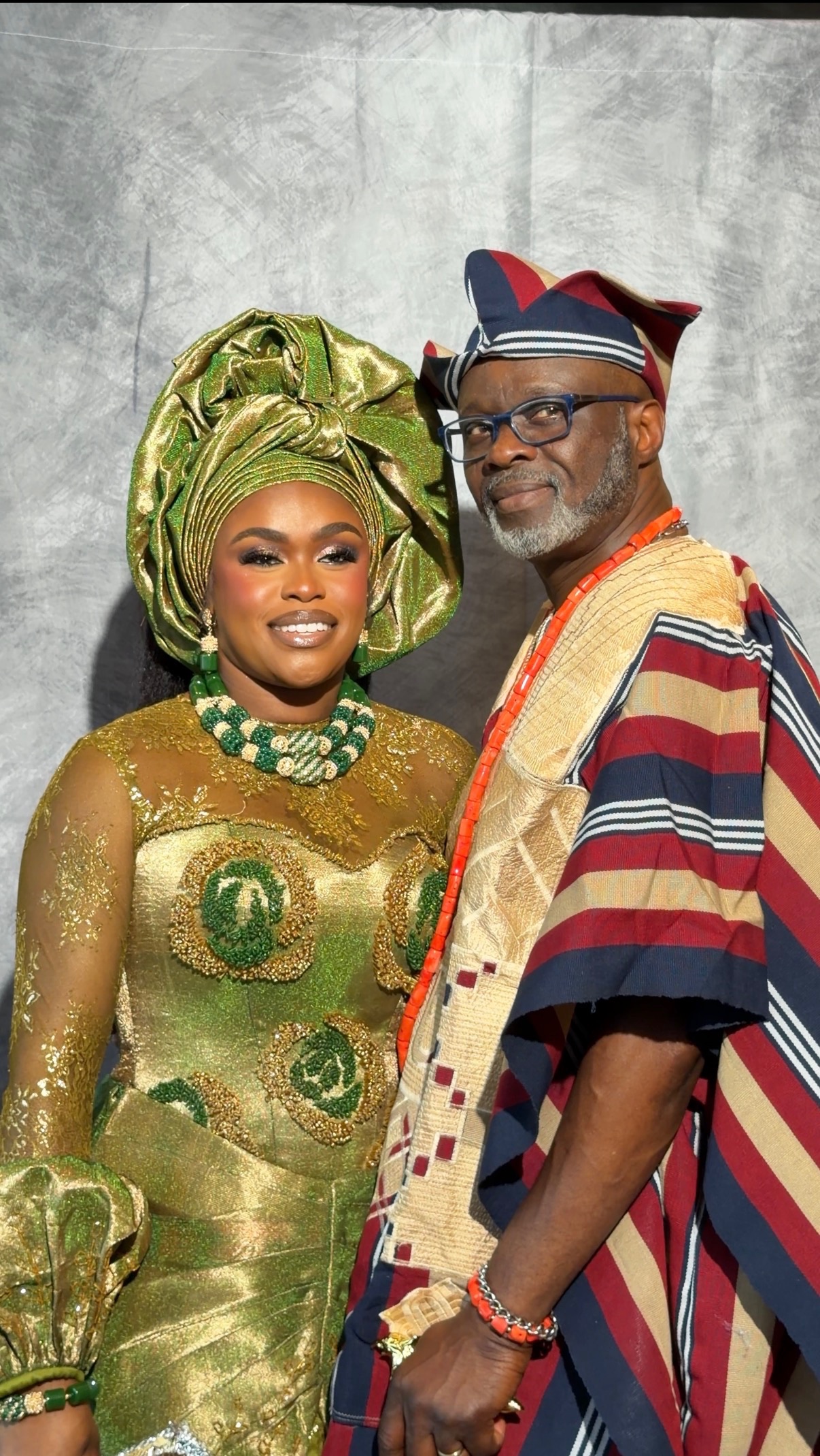 A bride in green and gold standing beside a guest in traditional attire