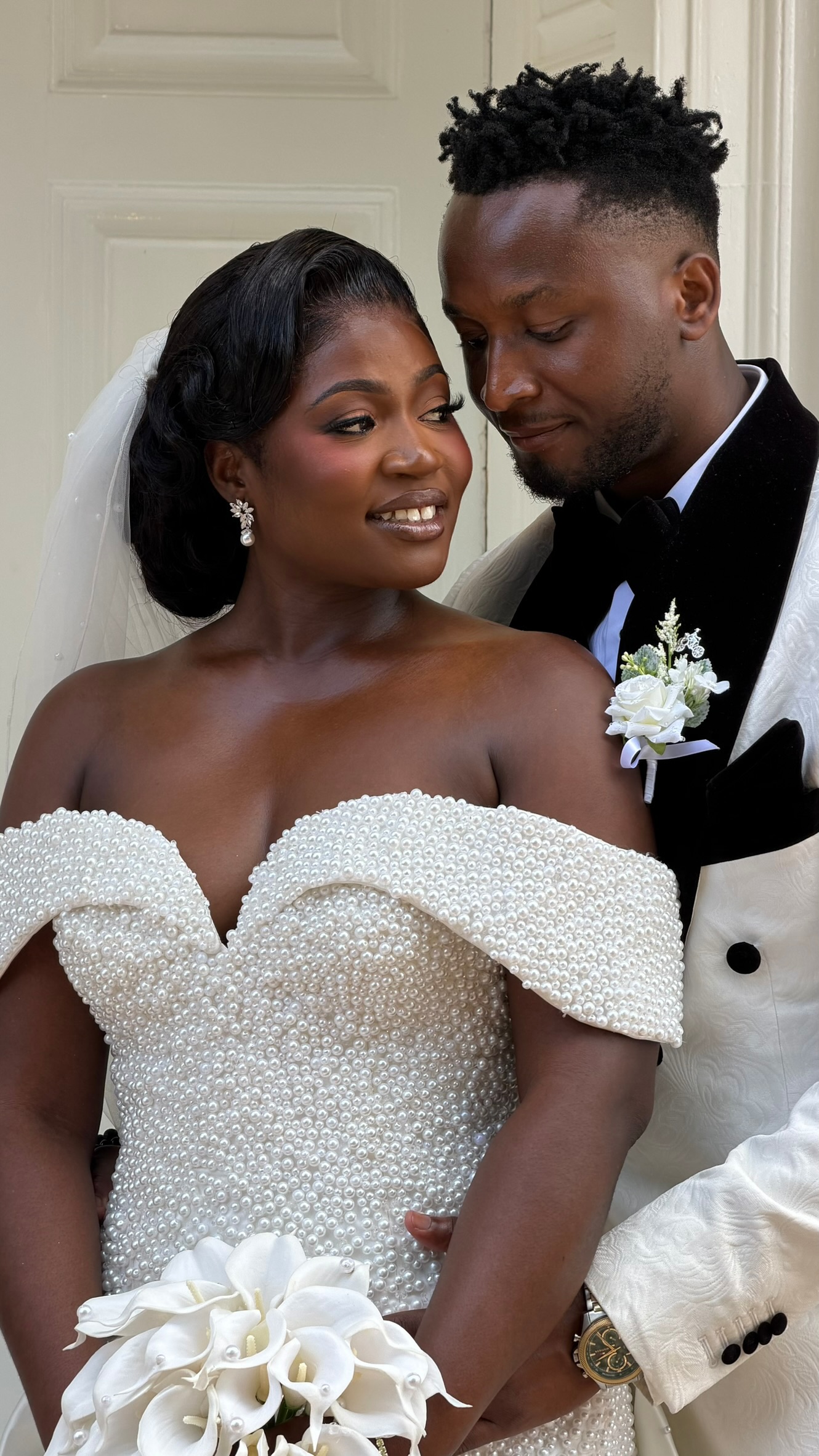 A bride holding white calla lilies with her groom beside her